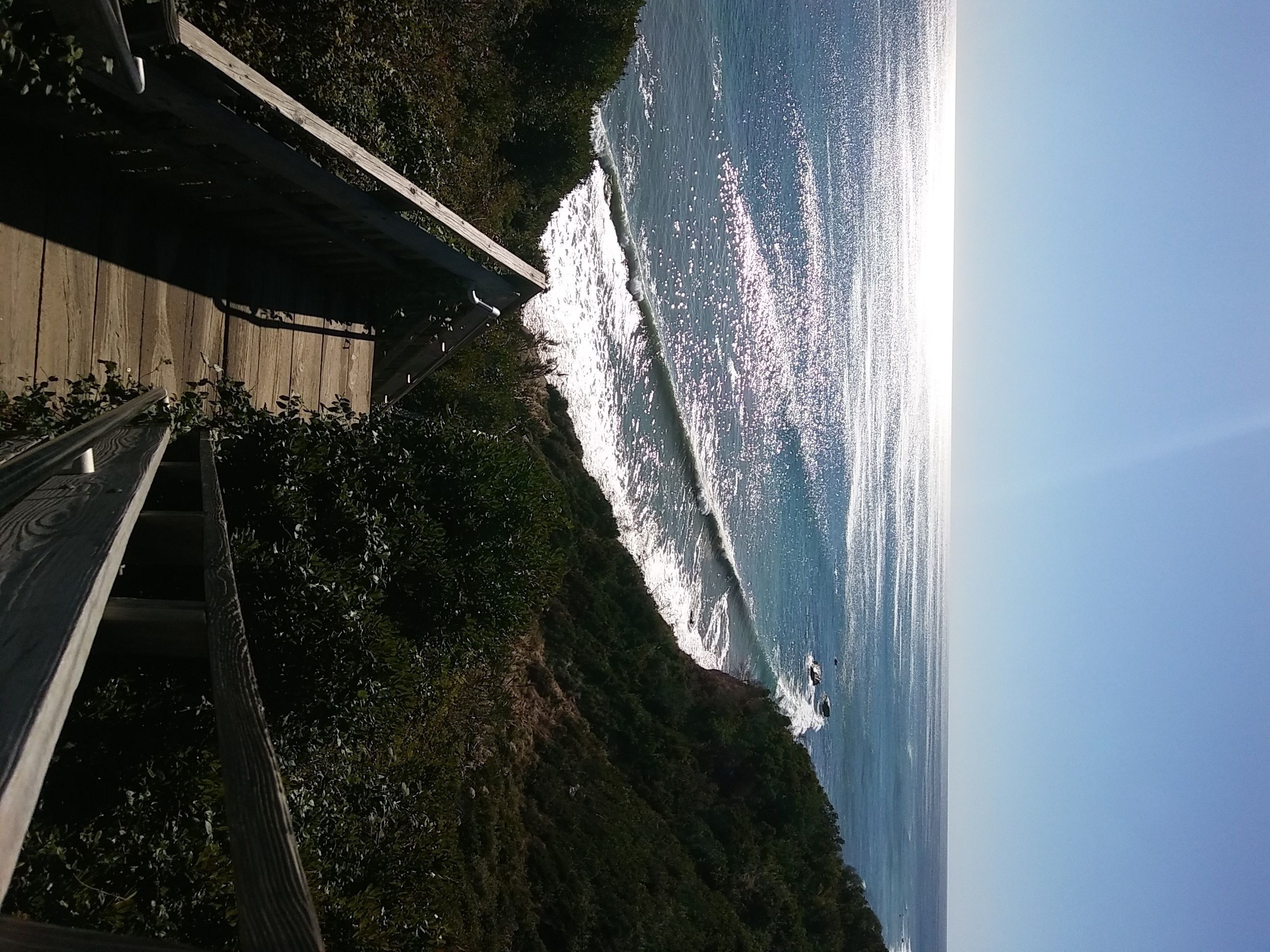 A wooden deck overlooking a coastal area with a view of the ocean and a clear sky.