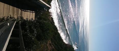 A wooden deck overlooking a coastal area with a view of the ocean and a clear sky.