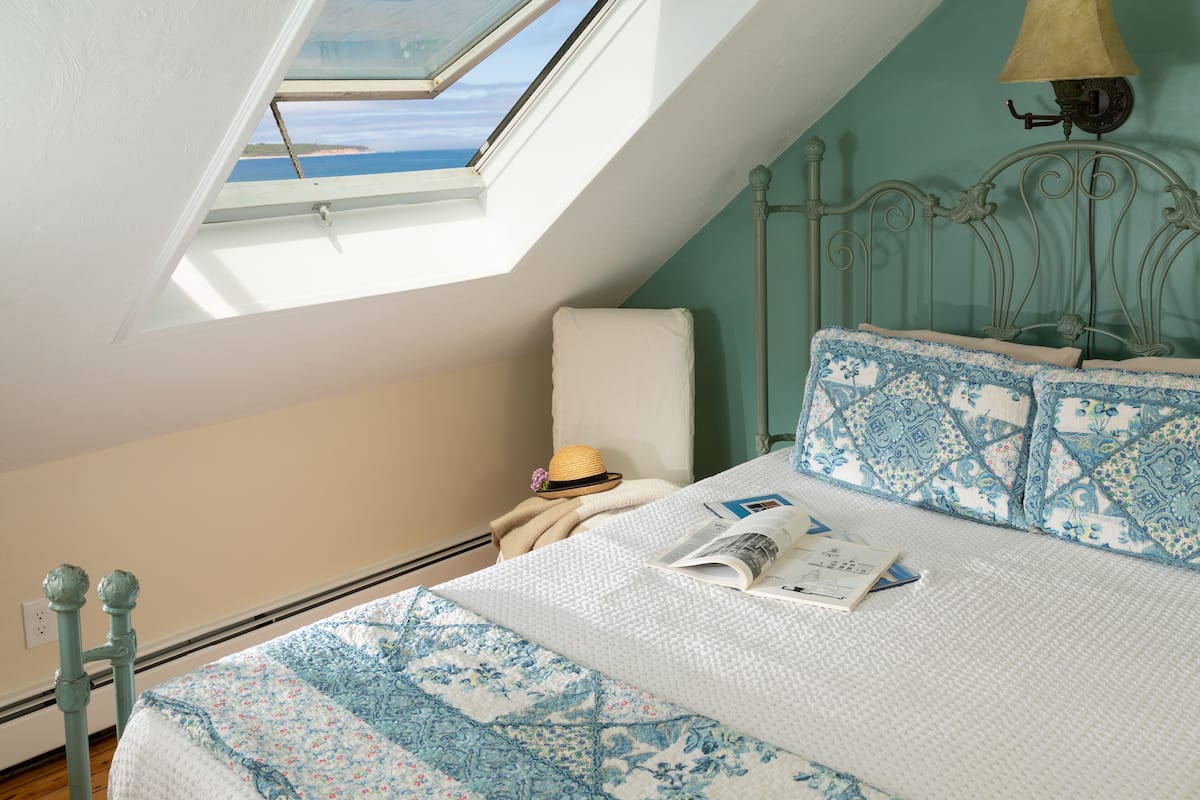 Une chambre avec un puits de lumière, un lit avec une literie à motifs, une lampe de chevet et un chapeau posé sur la table de chevet.