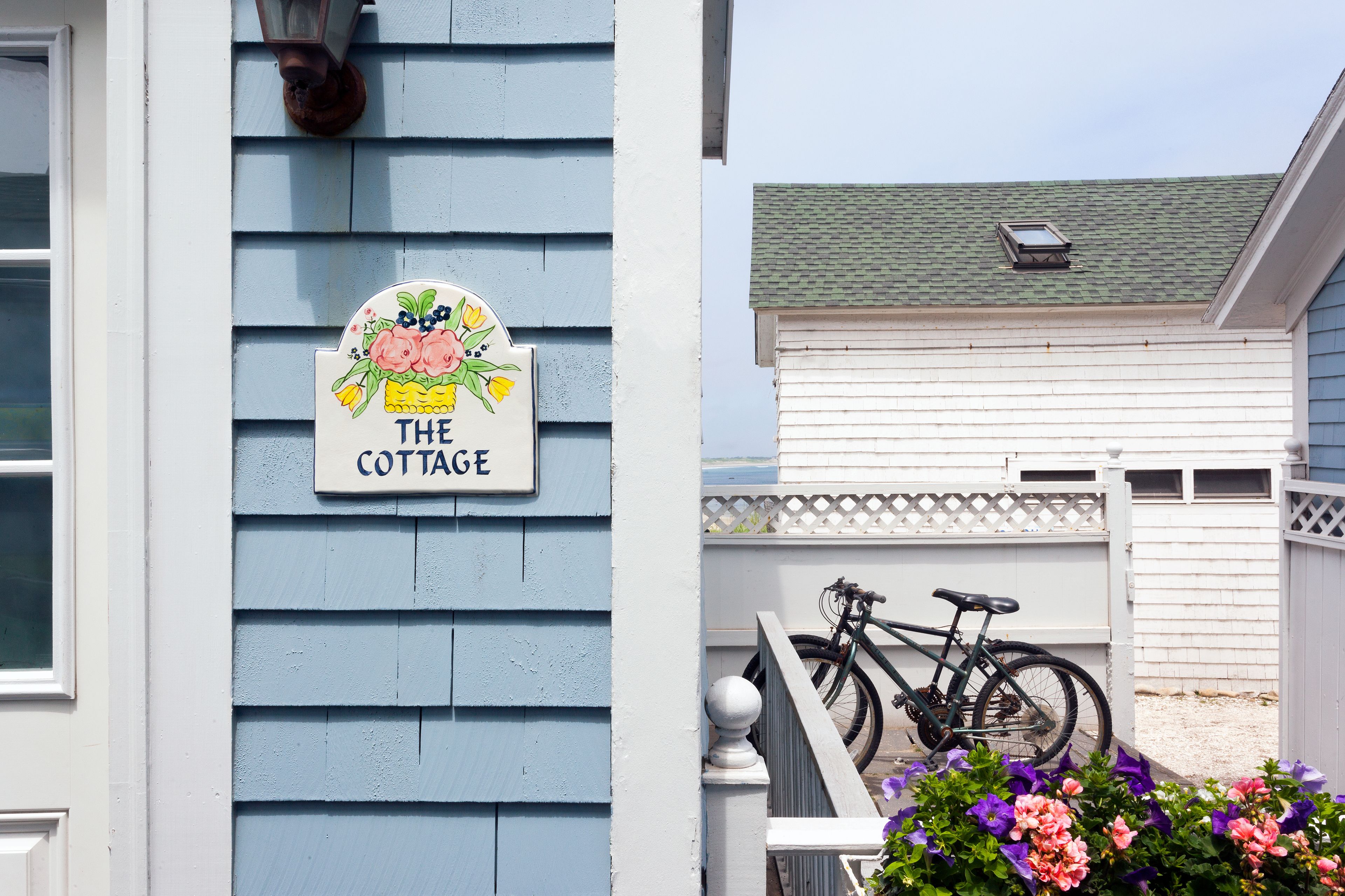 Un letrero de cabaña con decoración floral, una bicicleta y una cerca blanca.