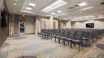 A conference room with rows of chairs, a carpeted floor, and a flat-screen TV on the wall.