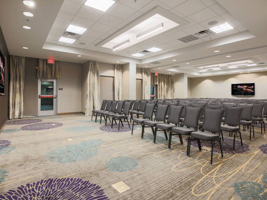 A conference room with rows of chairs, a carpeted floor, and a flat-screen TV on the wall.
