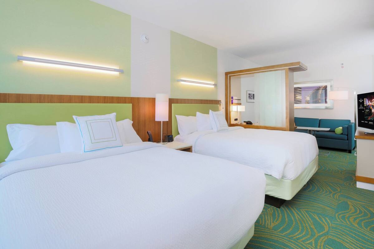 A hotel room with two beds, a sofa, a TV, and a bathroom mirror.