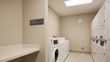 A laundry room with a washing machine, dryers, and a clock on the wall.