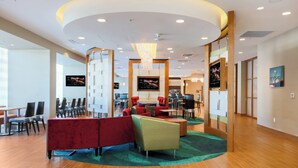 Un moderno vestíbulo de hotel con una zona de estar circular, varias televisiones y suelo de madera.