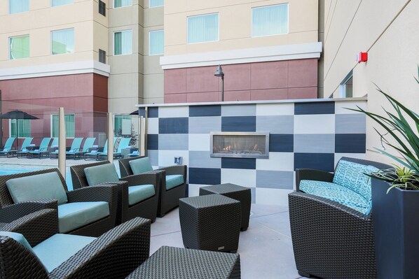 Un patio de hotel con muebles de mimbre, un muro a cuadros y una piscina al fondo.