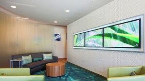 Un moderno vestíbulo de hotel con un sofá modular, una mesa de centro redonda de madera y un televisor grande montado en la pared.