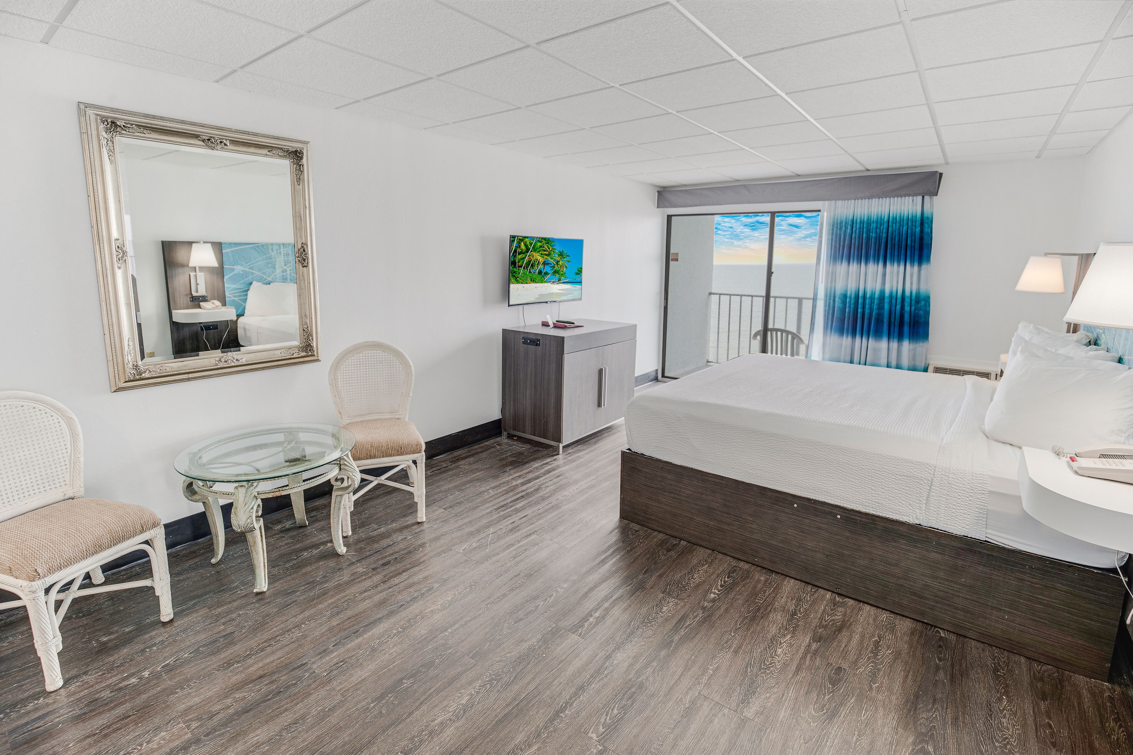 A hotel room with a large bed, a desk, a chair, a small table, and a TV.