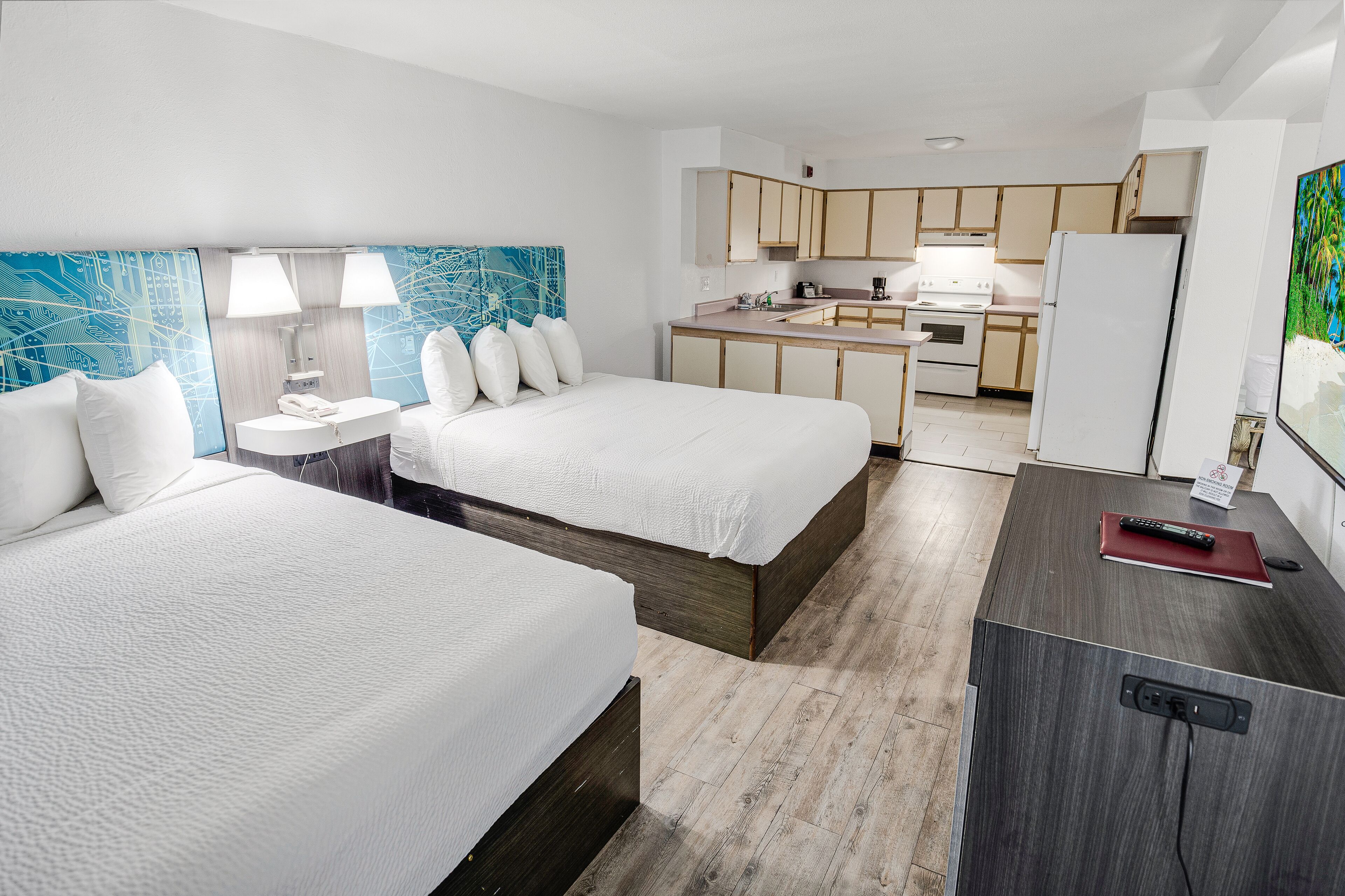 A hotel room with two beds, a small kitchenette, and a bathroom with a blue abstract painting.