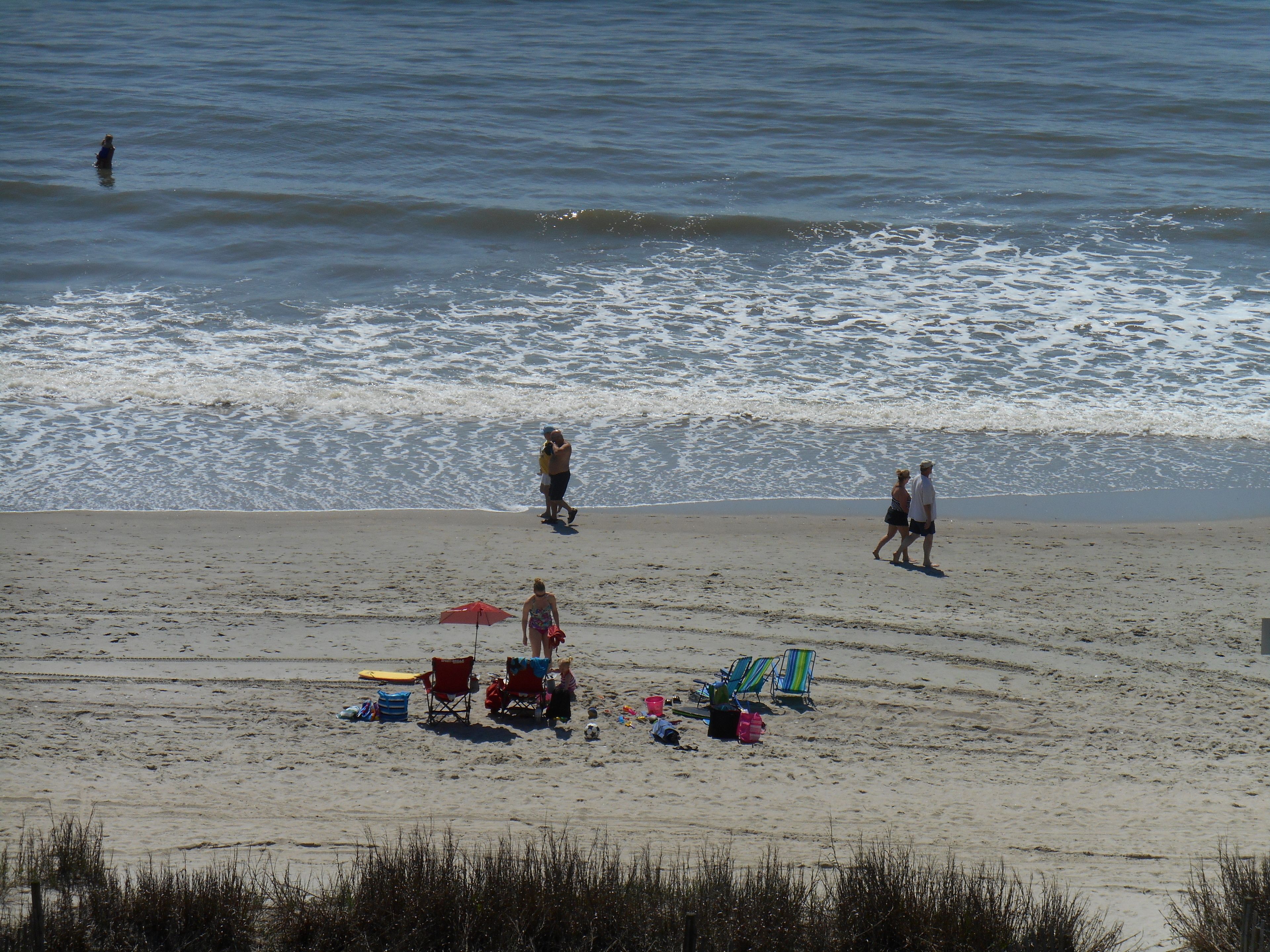 A beach with people walking, a surfboard, and beach chairs.