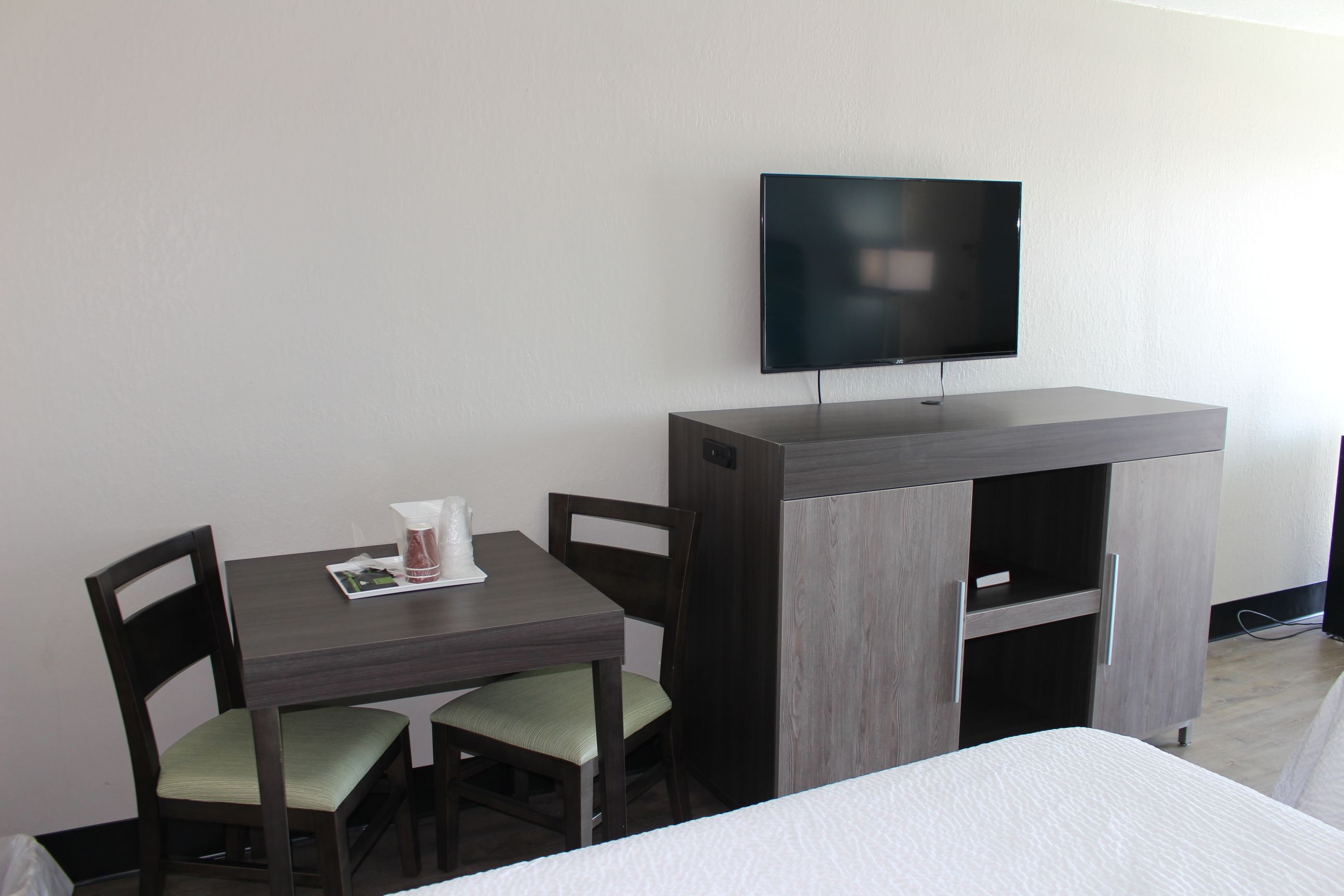 A hotel room with a bed, a desk with a chair, a television mounted on the wall, and a wardrobe.