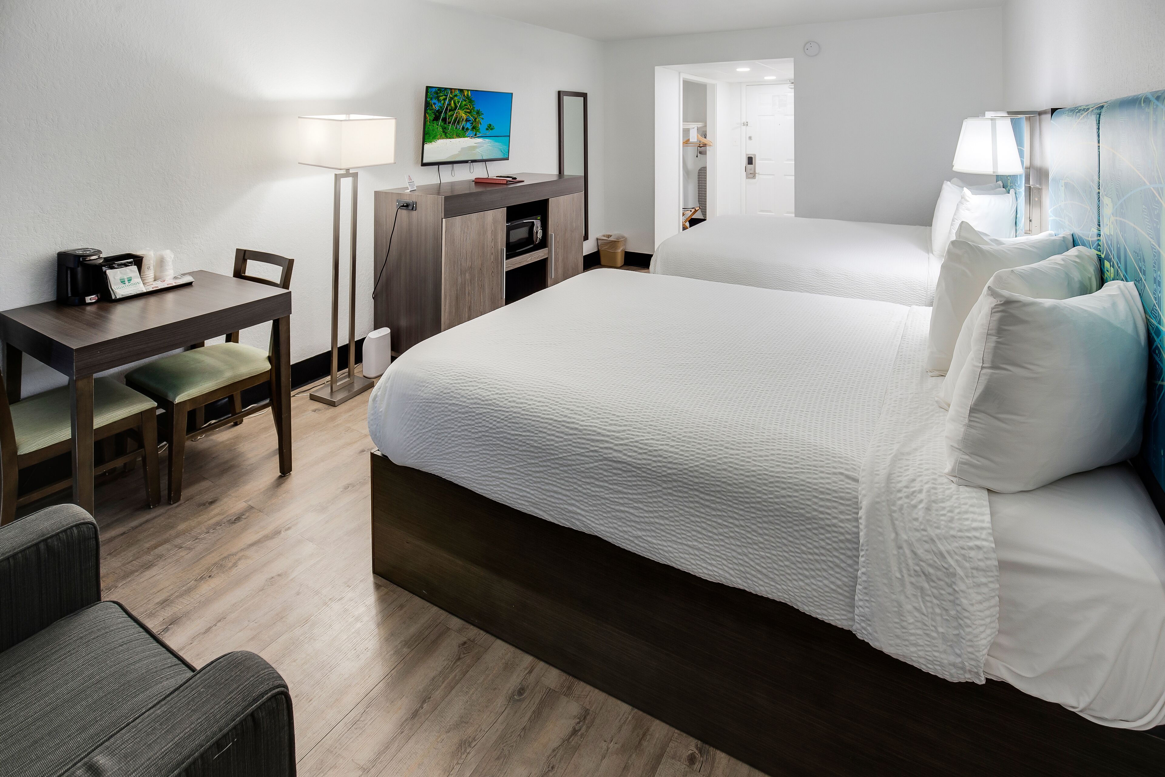 A hotel room with a large bed, a desk with a computer, a TV, and a lamp.