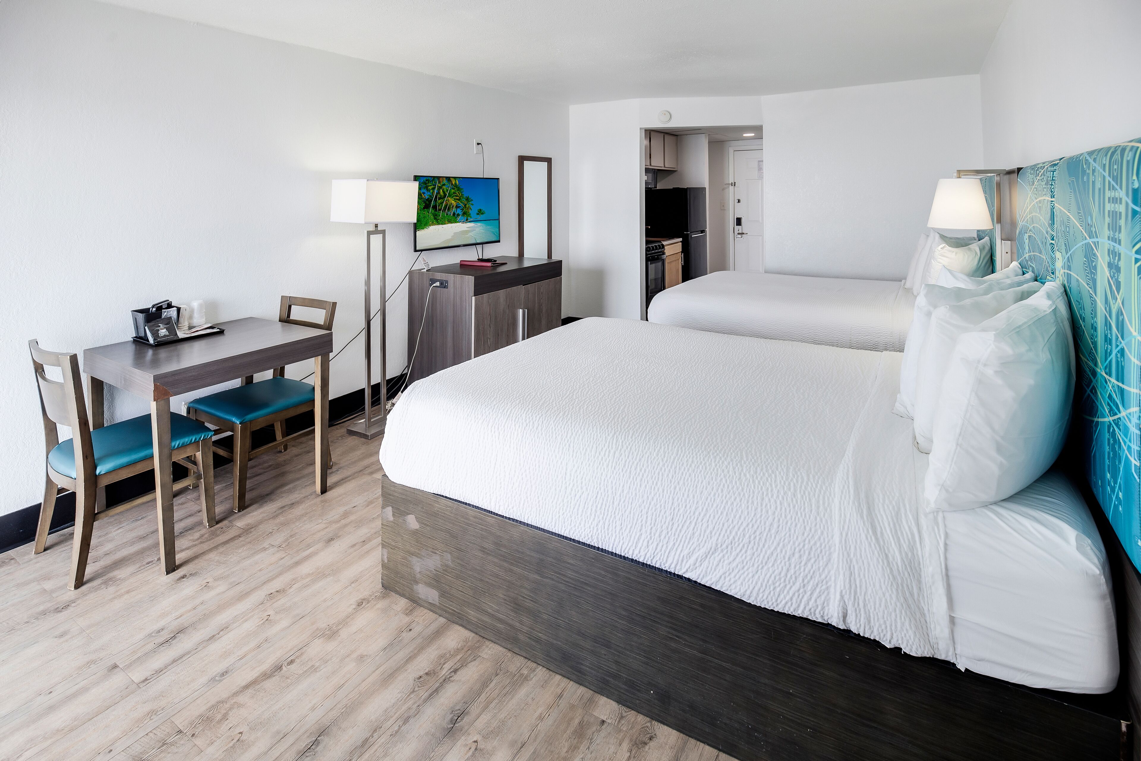 A hotel room with a bed, a desk with chairs, a TV, and a kitchenette.