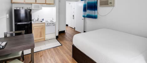 A compact hotel room with a bed, a small kitchenette, a dining table, and a wooden floor.