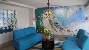 A modern living room with a blue sofa set, a round coffee table with a plant, a striped rug, and a large wave-themed mural on the wall. - Tropical Seas Hotel (Myrtle Beach)