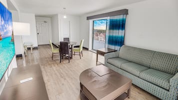 Una sala de estar moderna con un sofá, una mesa de centro, una mesa de comedor con sillas y un ventanal con cortinas.