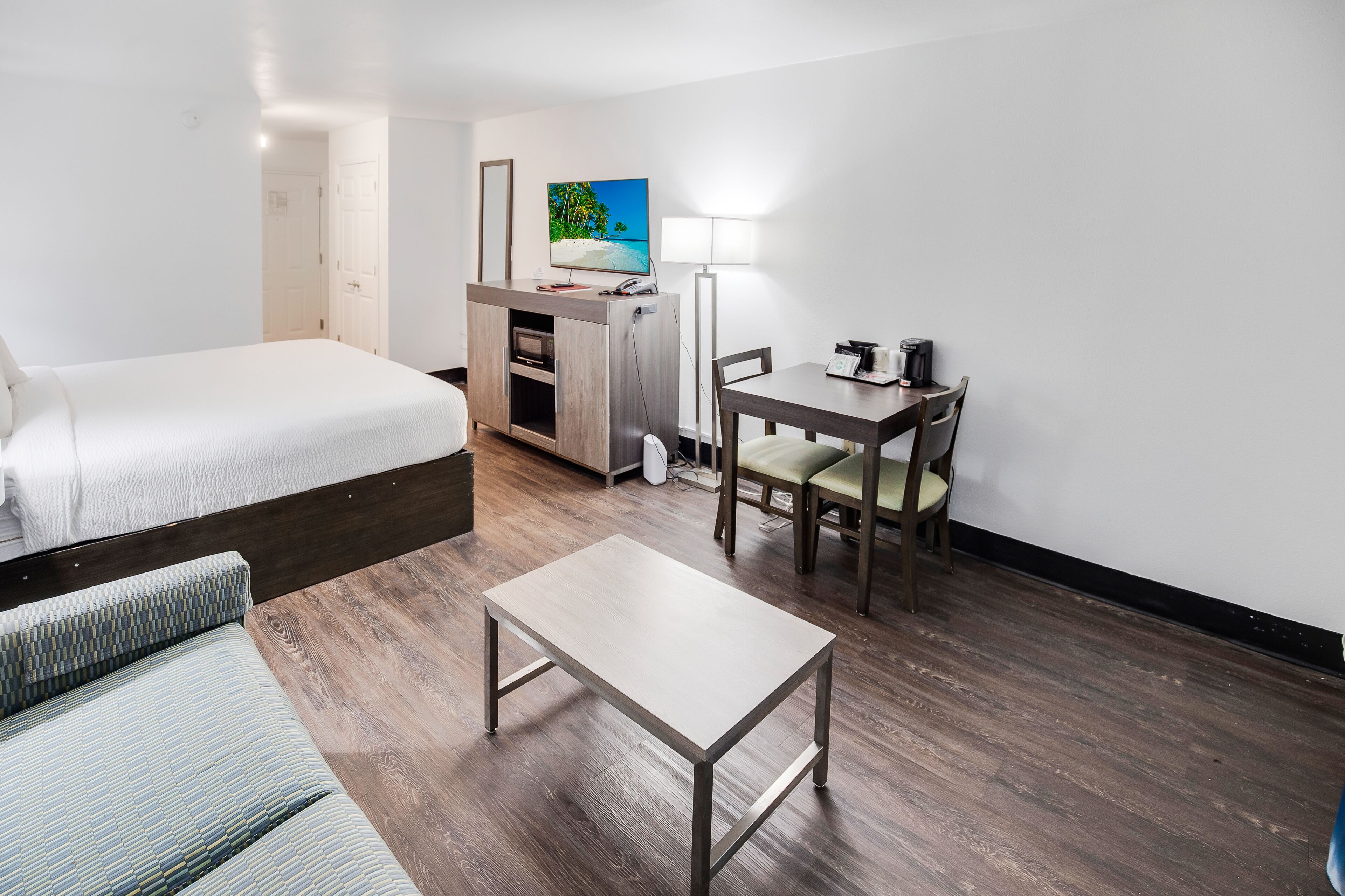A hotel room with a bed, a desk, a chair, a table, and a TV.
