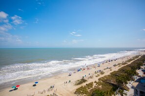 A beach with a wooden walkway, beach umbrellas, and a pier in the background. - Tropical Seas Hotel (Myrtle Beach)