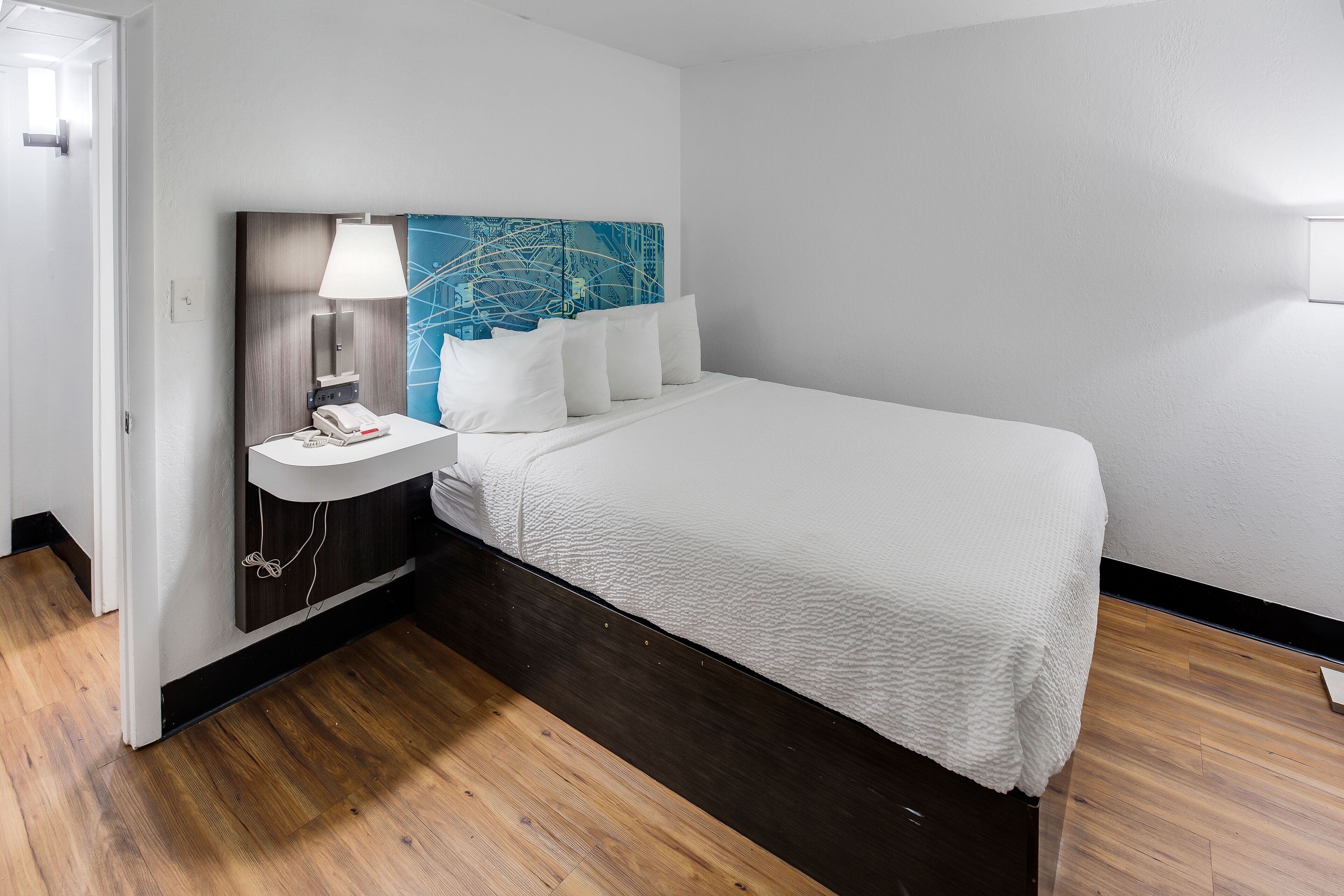 A hotel room with a bed, a bedside table with a lamp, a phone, and a wall-mounted artwork.