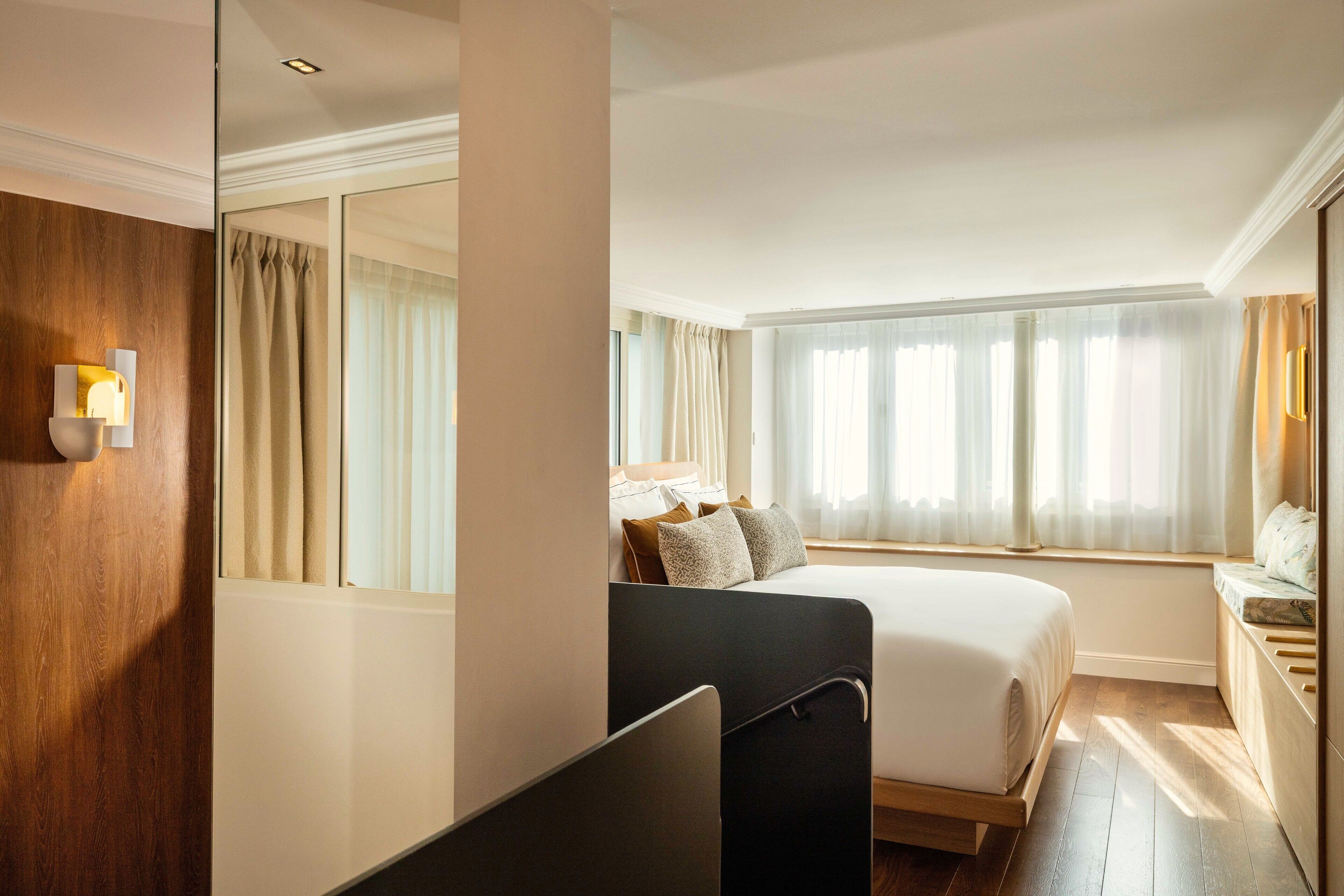 A hotel room with a bed, bedside table, and a large window with curtains.