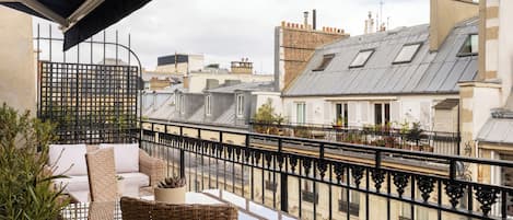 A balcony with wicker furniture, a view of neighboring buildings, and a metal railing.