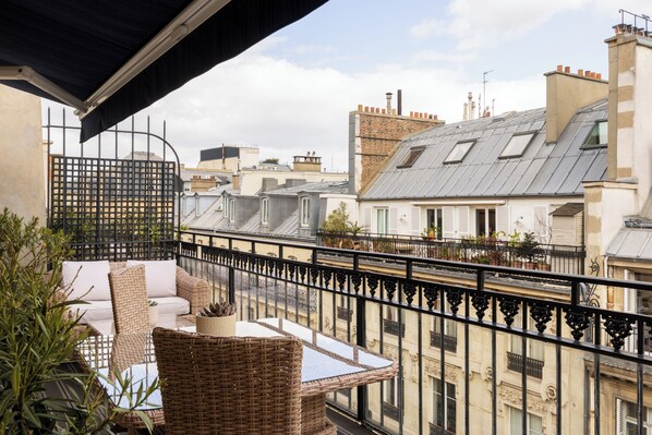 A balcony with wicker furniture, a view of neighboring buildings, and a metal railing. - Hotel & Spa Royal Madeleine (Paris)
