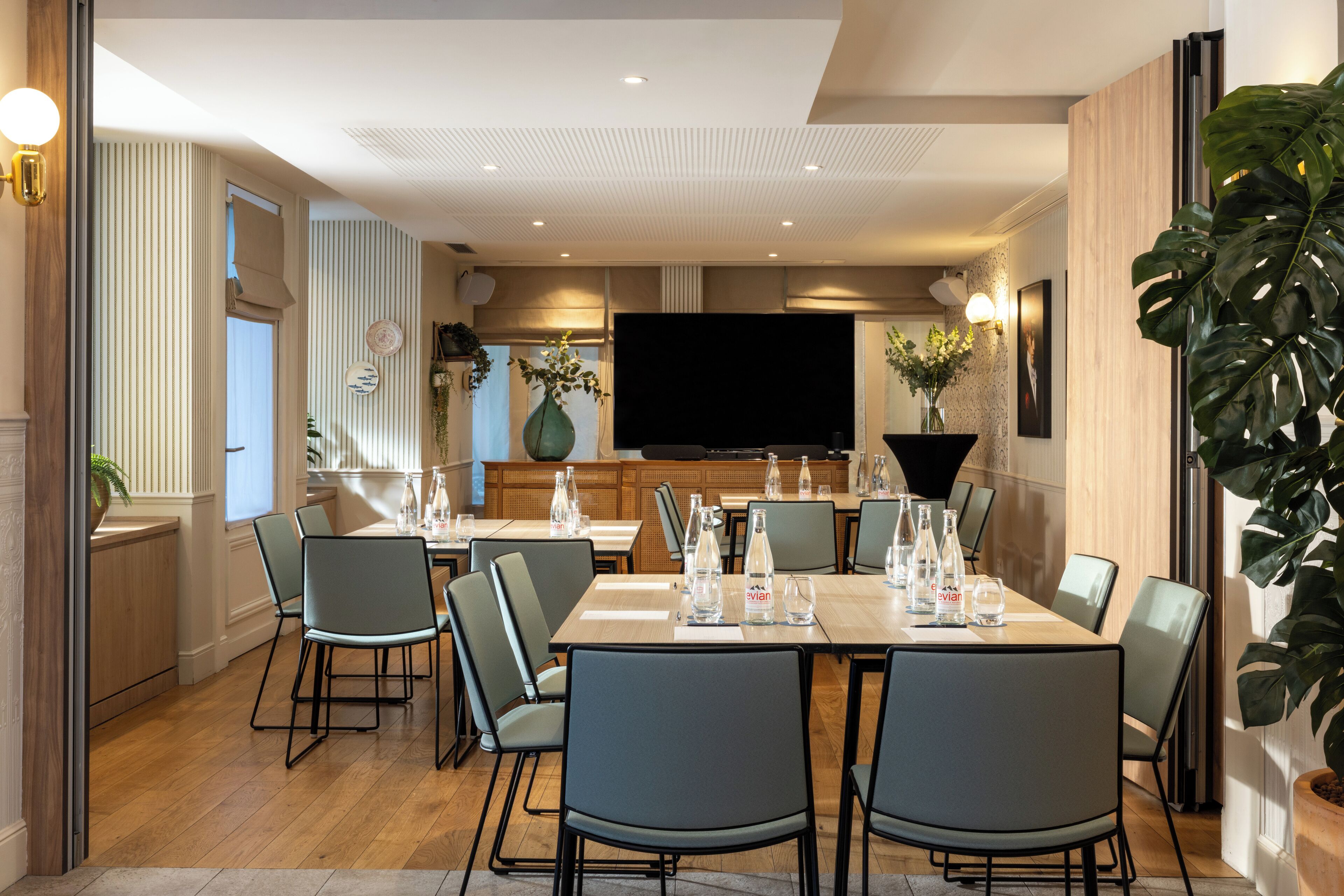 A modern dining area with a long table, multiple chairs, and a television in the background.