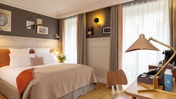 Una camera d'albergo con un letto, una scrivania con una lampada, una sedia, una macchina per il caffè e una finestra con tende.