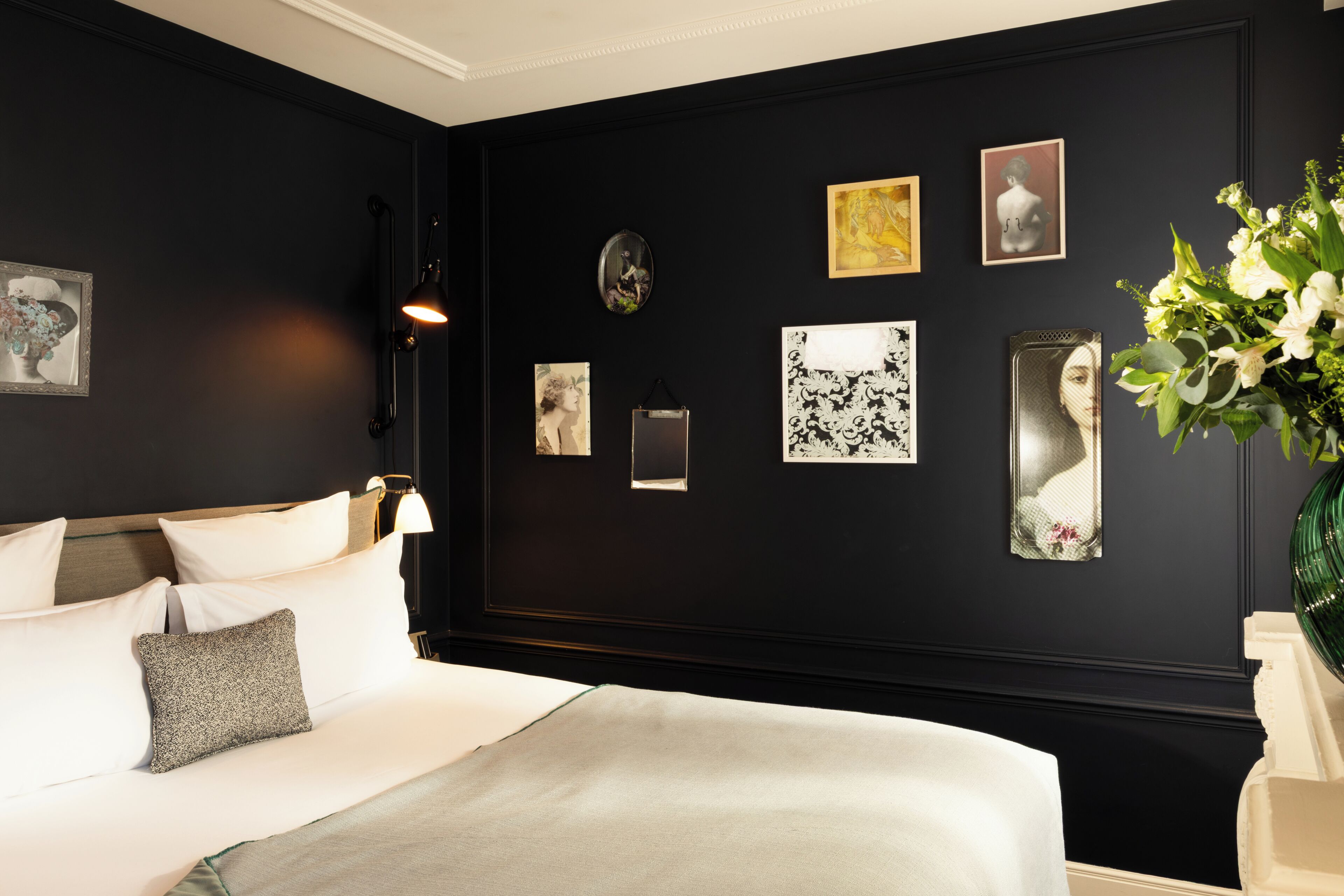 Un dormitorio con cama, mesita de noche, lámpara de pared y cuadros enmarcados.