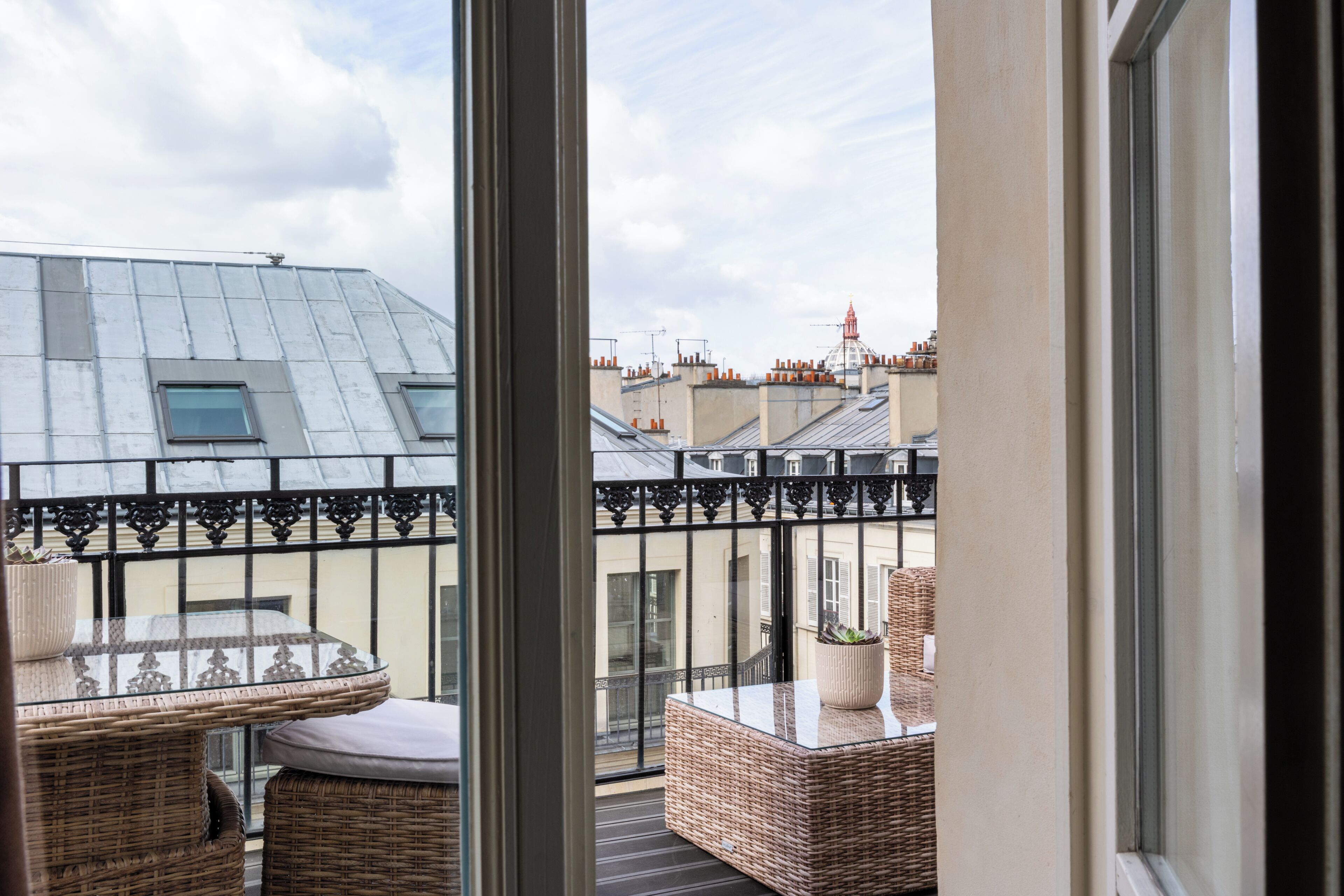 A balcony with wicker furniture, a glass balustrade, and a view of neighboring buildings.