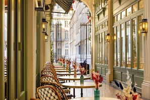 A corridor with rows of tables and chairs, each with a vase of flowers. - Hotel & Spa Royal Madeleine (Paris)