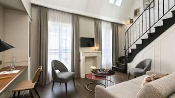 Een moderne woonkamer met een open haard, twee fauteuils, een bank, een eettafel met stoelen en een trap.