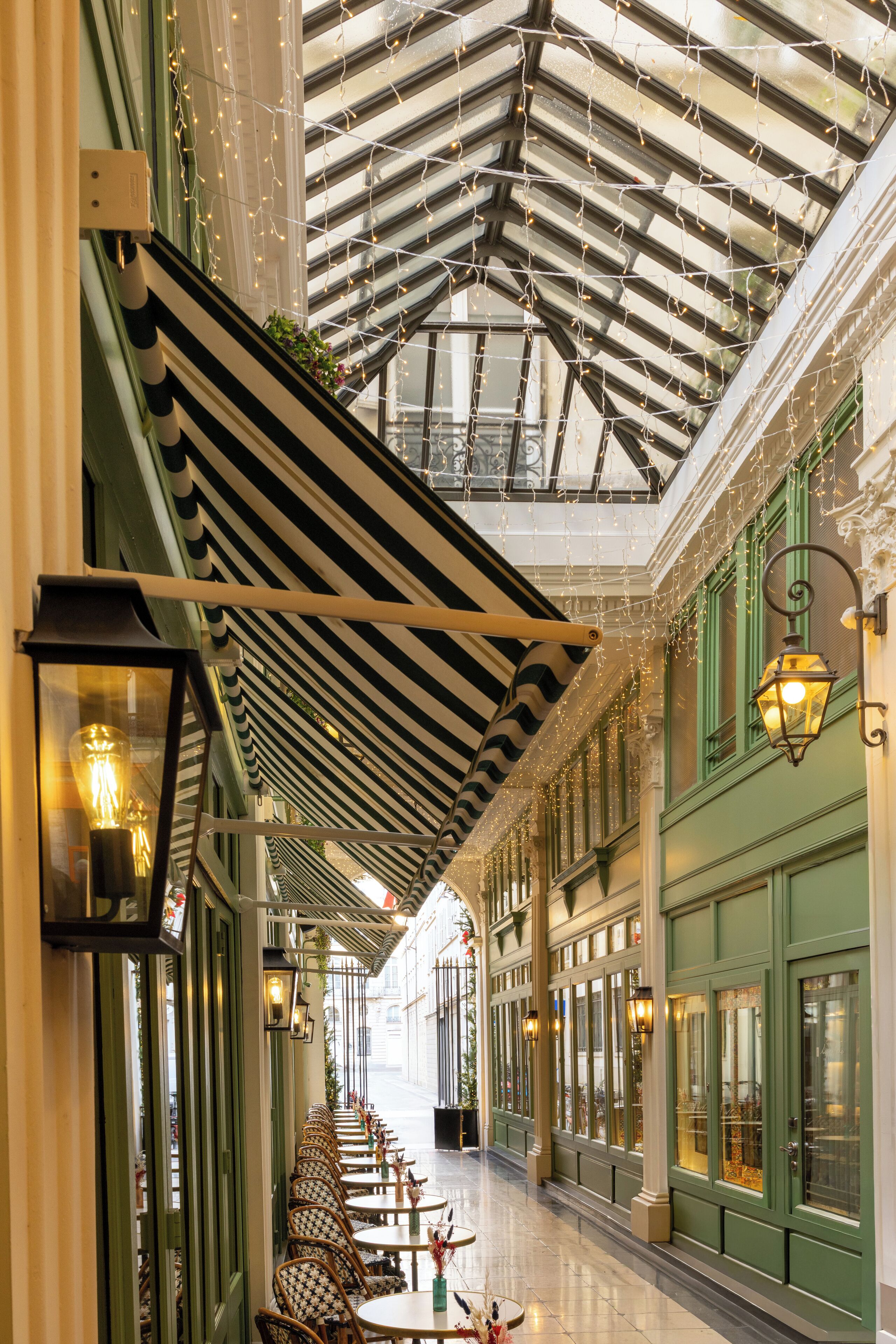 A covered outdoor seating area with tables and chairs, a glass ceiling, and green-painted walls.