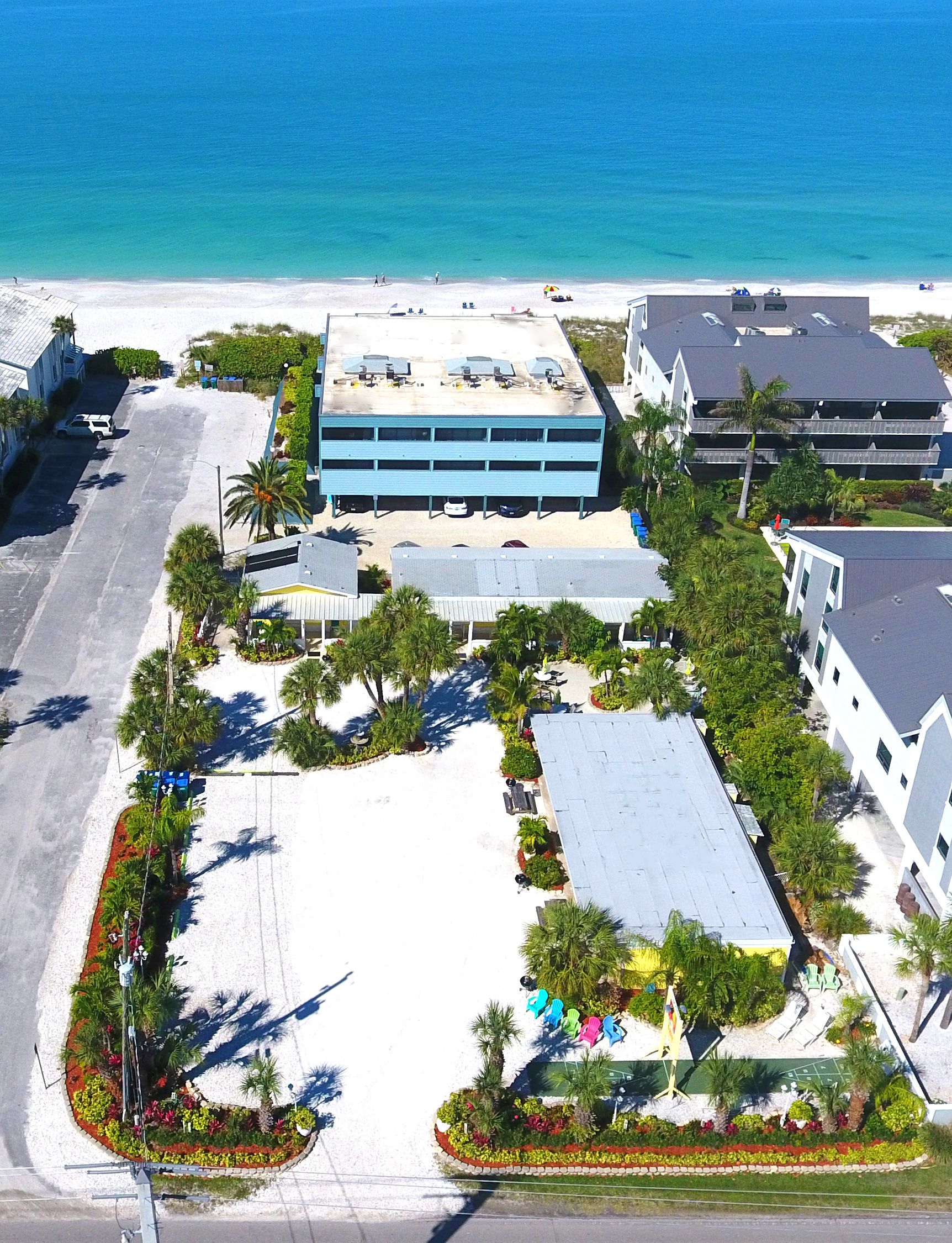 An aerial view of a hotel with a parking lot, a beach, and a parking garage.