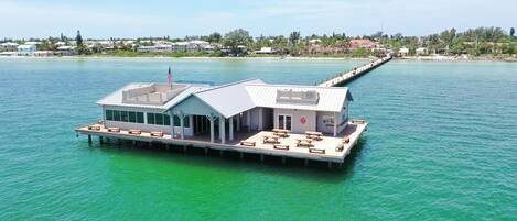 A waterfront houseboat with a covered deck, outdoor seating, and a flagpole.