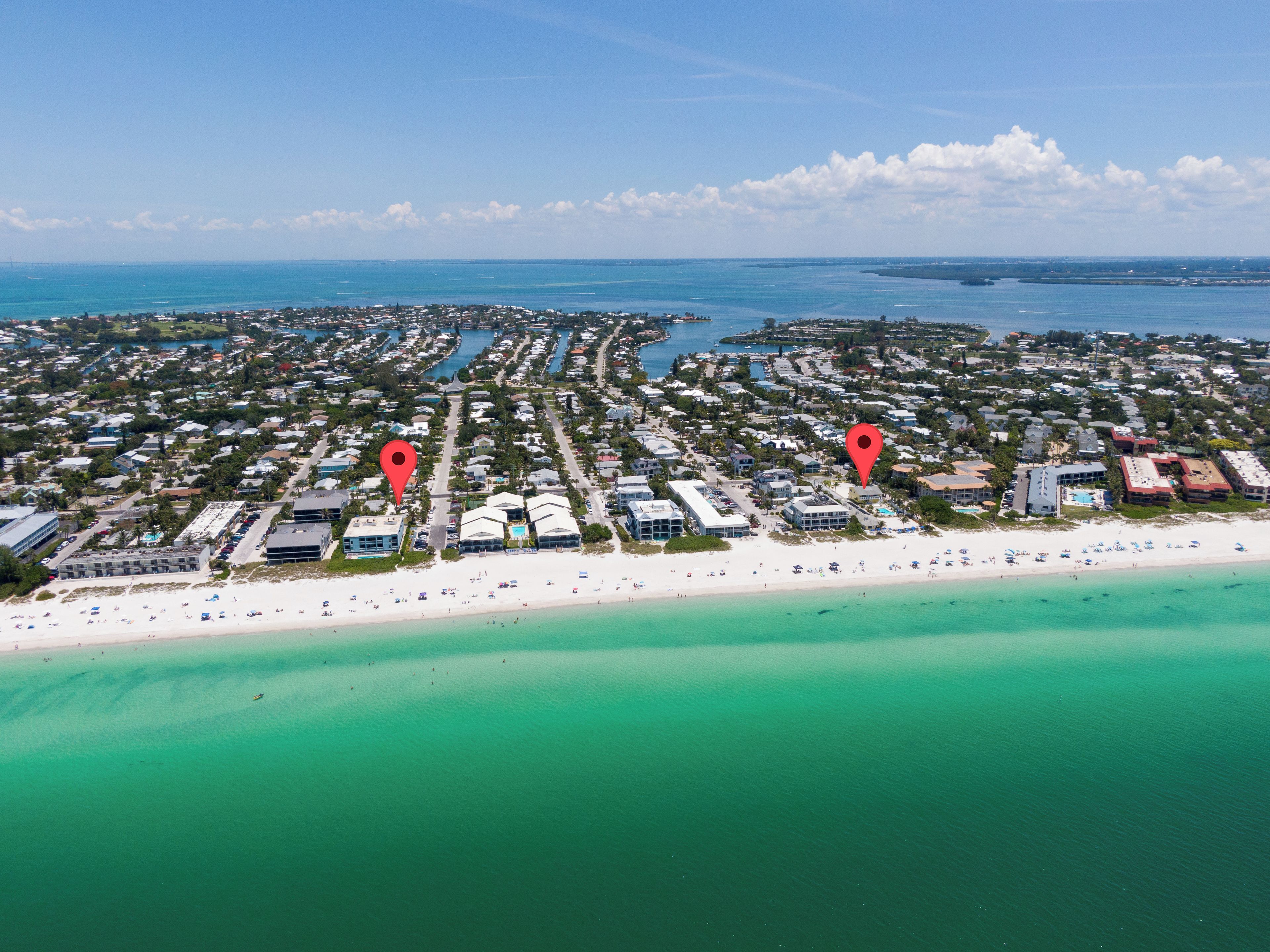 An aerial view of a coastal area with a beach, clear blue waters, and a dense residential area with marked locations.