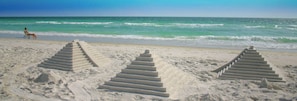 A beach with three stone staircases leading into the water, a person sitting on a beach chair, and the ocean in the background. - Tropical Breeze Beach Club (Holmes Beach)
