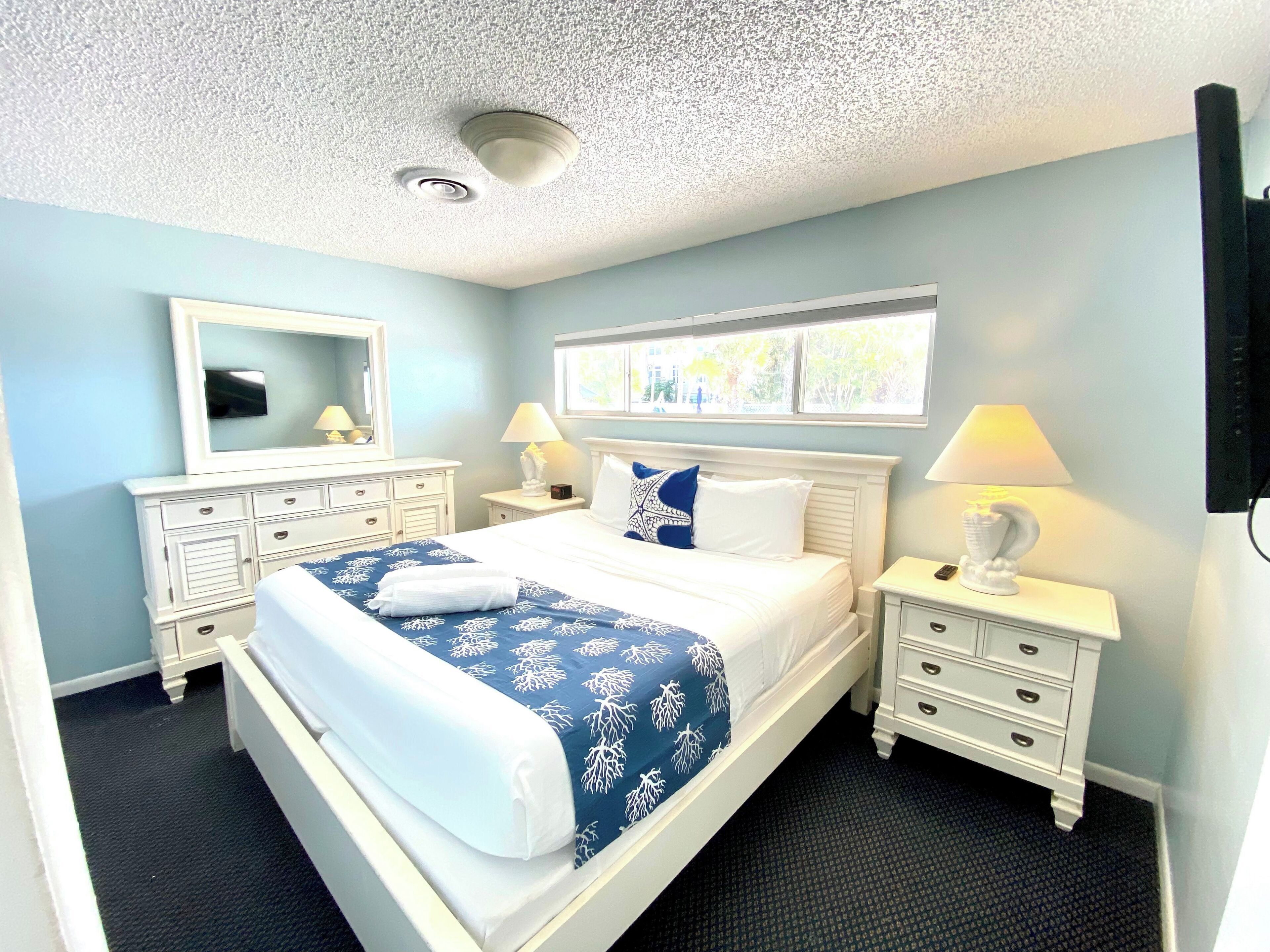 A hotel room with a bed, two nightstands, a dresser, a mirror, and a window with a view.