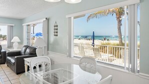 Quarto com mesa e cadeiras de vidro, sofá de couro, abajur e vista para a praia.