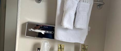 A bathroom with a towel rack holding two towels, a glass shelf with toiletries, and a mirror.