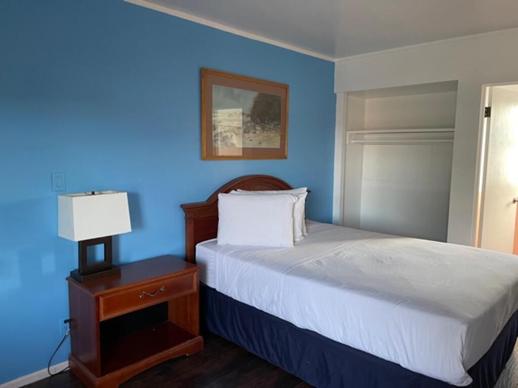 A hotel room with a bed, a nightstand, a lamp, and a painting on the wall.