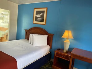 A hotel room with a bed, a nightstand with a lamp, a framed picture on the wall, and a bathroom visible through an open door. - Ephrata Inn Motel (Ephrata)