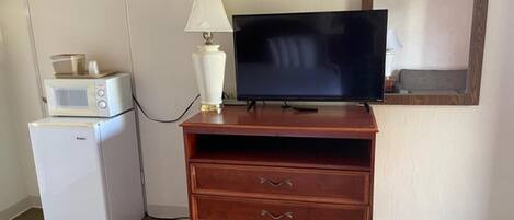 A kitchenette with a microwave, a refrigerator, and a wooden TV stand with a flat-screen TV.