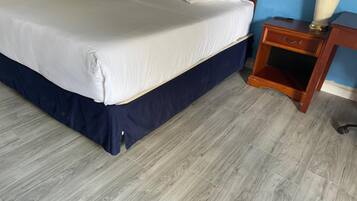 A bed with a white mattress and navy blue skirt, a wooden nightstand with a drawer, and a lamp.