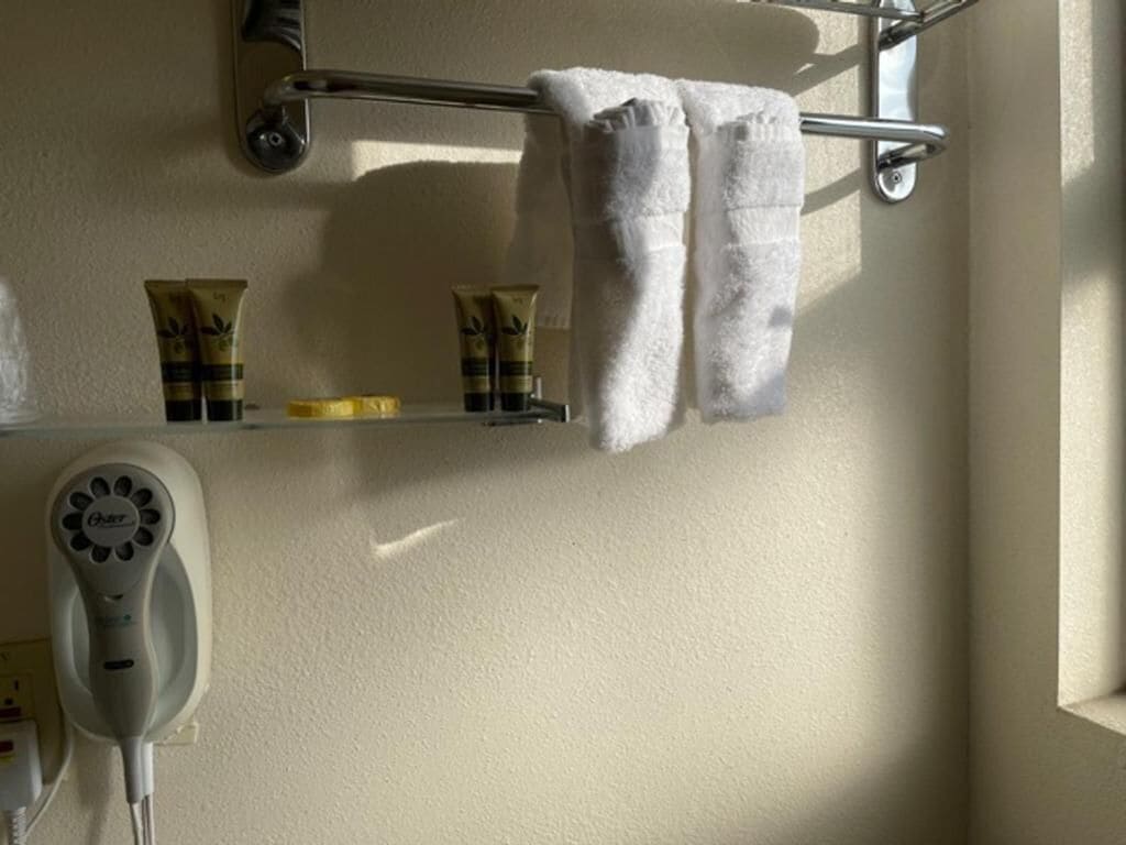 Een badkamer met een handdoekrek met twee handdoeken, een haardroger en toiletartikelen op een plank.