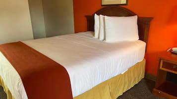 Una cama bien hecha con sábanas blancas y un plaid marrón, un cabecero de madera y una mesita de noche con una lámpara.