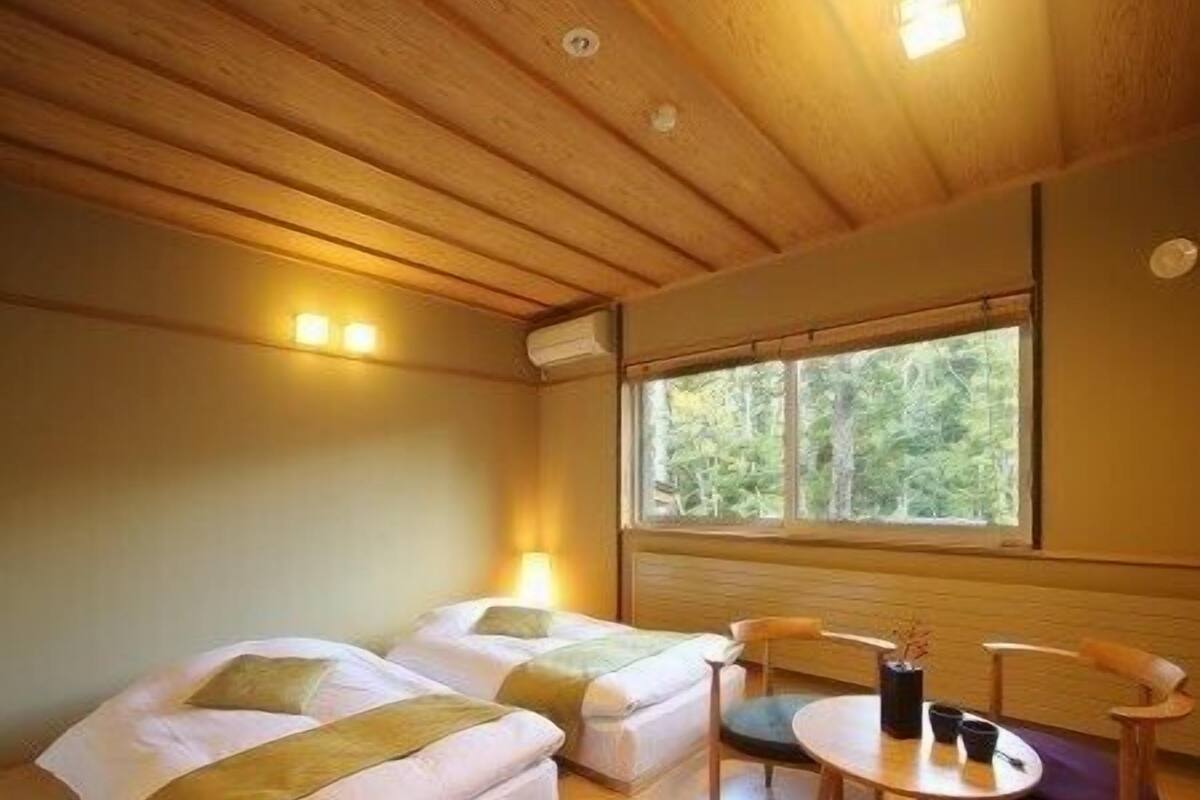 A room with two beds, a small table, and a window with a view of trees.