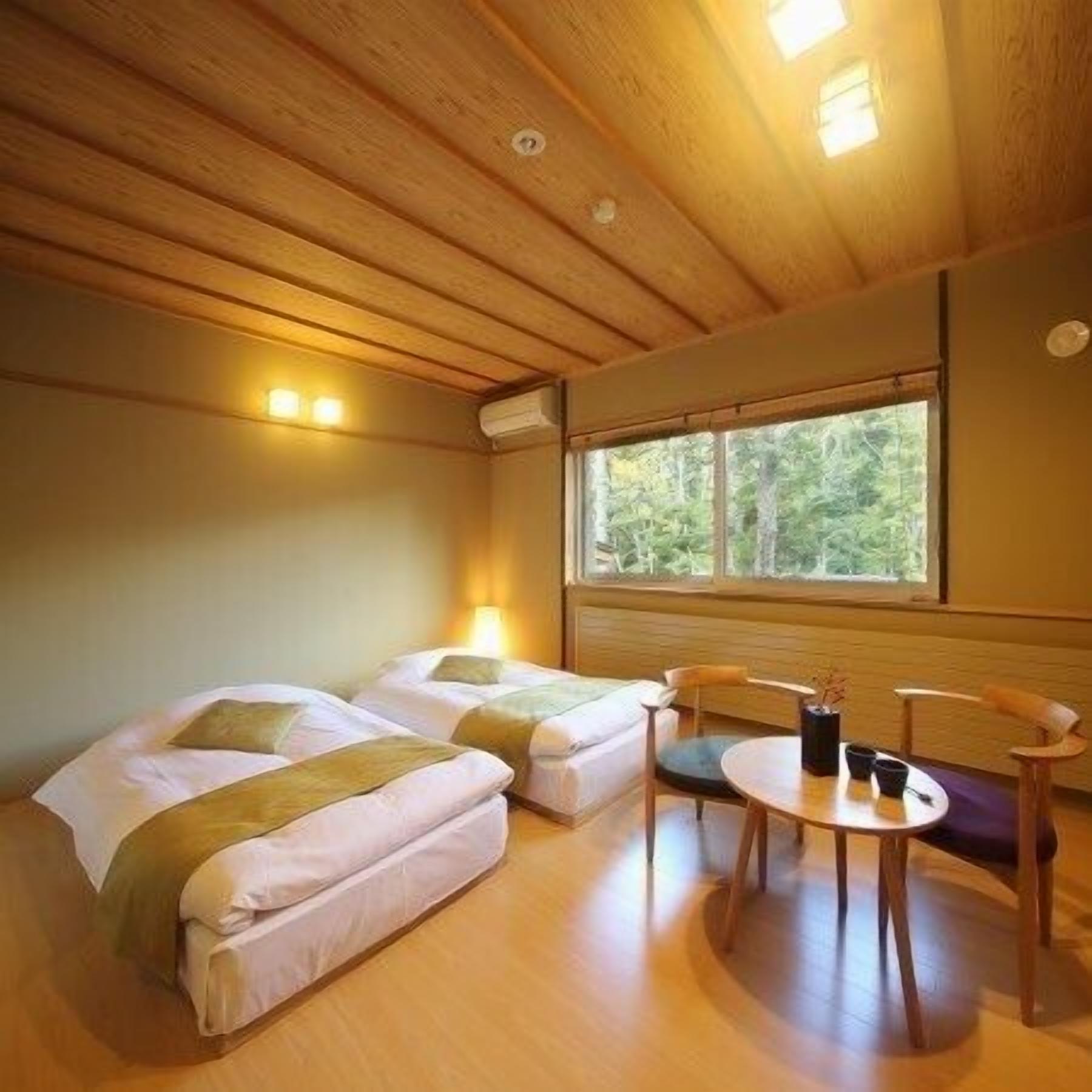 Une chambre avec deux lits, une table ronde et une fenêtre donnant sur les arbres.