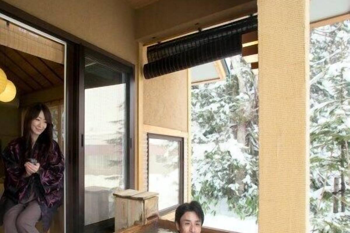 A traditional Japanese onsen with a wooden tub, a small wooden stool, and a view of snow-covered trees.