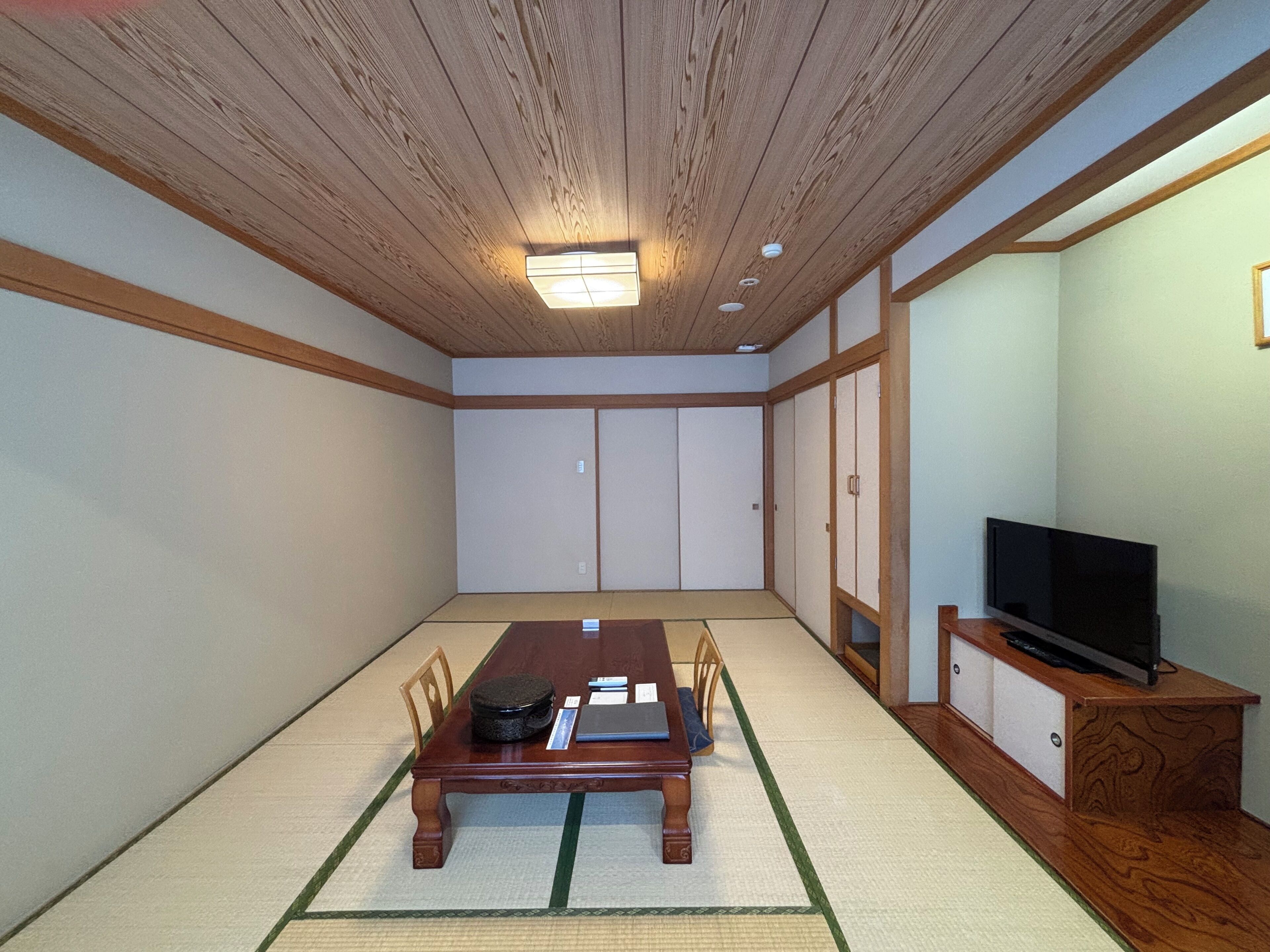 Um quarto japonês tradicional com tatames, teto de madeira baixo, portas deslizantes e uma televisão sobre suporte de madeira.